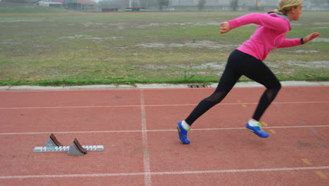 Seitenansicht-Einer-Kaukasischen-Sportlerin,-Die-Ihre-Startposition-Einnimmt-Und-Auf-Der-Strecke-Auf-Einer-Sportstätte-Läuft-