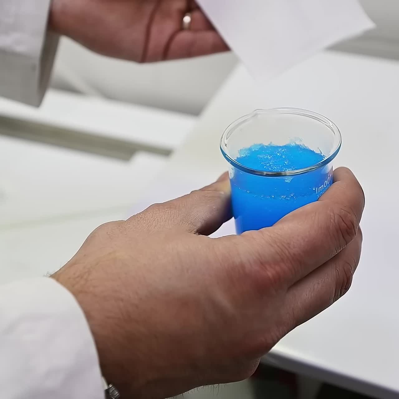 Male hand holding a beaker with blue staff from inside the diaper. Researcher testing the absorption with the help of a napkin. Close up