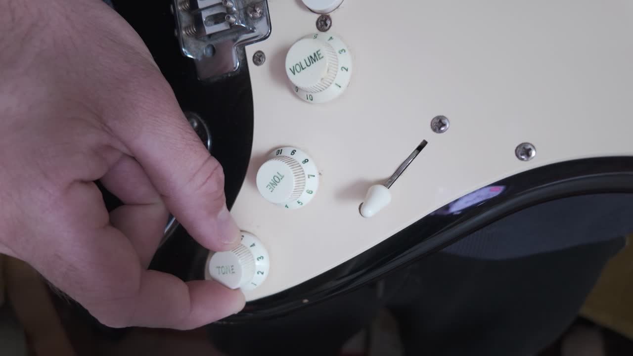 Close up of a musician's hand turning the volume knob on an electric guitar, setting the perfect sound