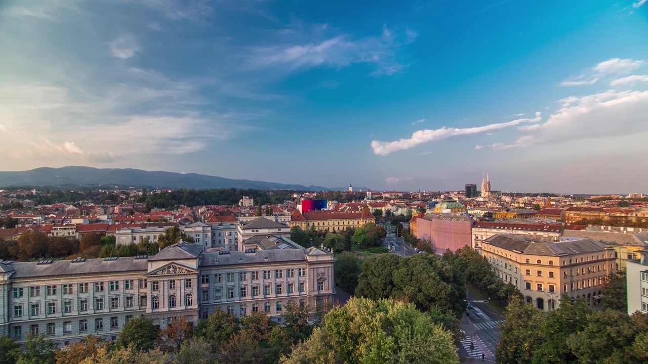Panorama do centro da cidade em timelapse filmado do alto de um arranha-céu com o cruzamento em frente ao teatro nacional e museu em Zagreb, Croácia. Vista aérea antes do pôr do sol