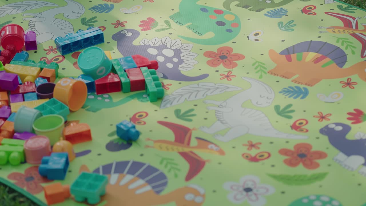 Juguetes de plástico de colores brillantes esparcidos sobre una alfombra de juego de dinosaurios en el exterior