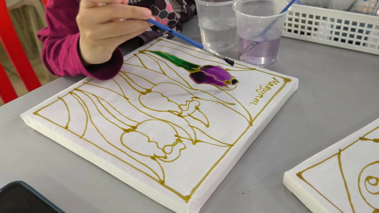 Close-up of a child painting colorful dye on a traditional Malaysian batik canvas. Young student learning cultural heritage craft through hands-on art. Educational activity introducing authentic folk