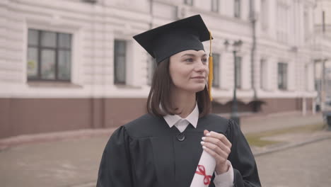 estudiante de posgrado de linda chica en vestido y gorra con diploma mirando a la cámara y sonriendo