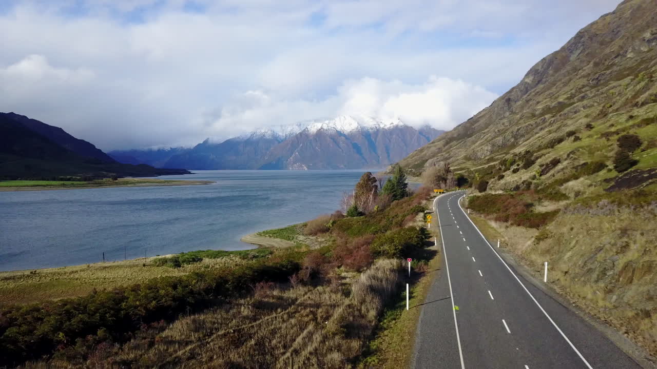 Aerial shot with grass next to a road with Snowy mountains in the background. New Zealand