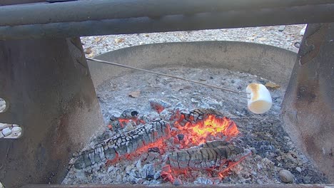 large white marshmallow turning brown while roasting over a campfire