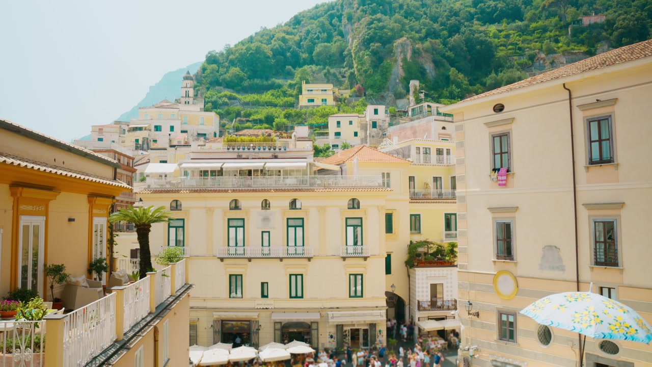 Palma e edificio giallo che si affacciano su una vivace piazza turistica ad Amalfi