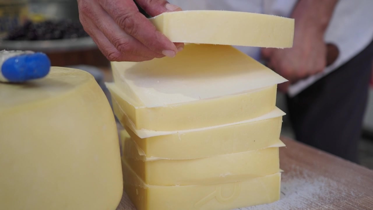 Casaro che affetta blocchi freschi di formaggio a un mercato