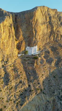 the panagia hozoviotissa monastery on steep cliffside above sea at golden hour sunlight, amorgos island, aerial shot, vertical