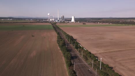 Vías-De-Tren-En-Medio-De-Los-Campos-Que-Conducen-A-Una-Central-Eléctrica-De-Carbón-En-La-Distancia