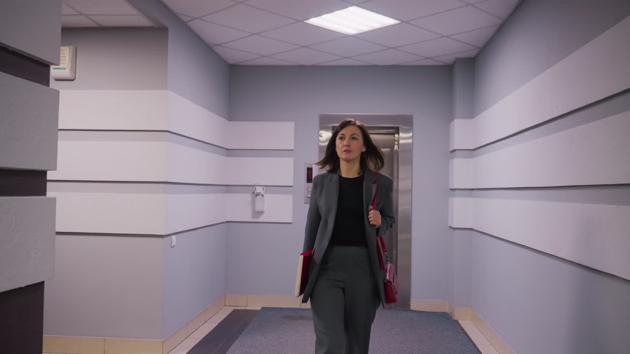 Professional woman walking down office corridor, carrying red folder and heading toward elevator in modern business building. Clean, minimalist design ideal for corporate, business, or office use