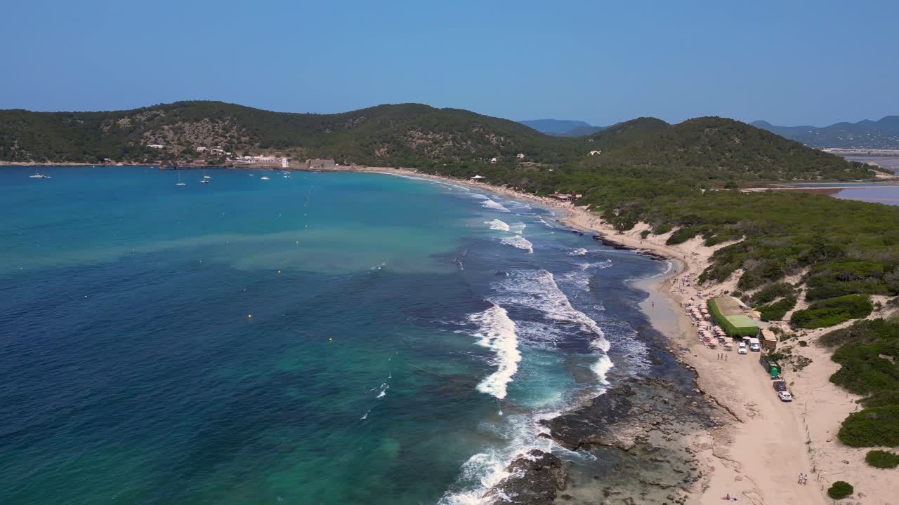 Onde turchesi che si infrangono sulla costa rocciosa della spiaggia di Ses Salines con l'antica torre di avvistamento. Spettacolare ripresa aerea con drone dall'alto.