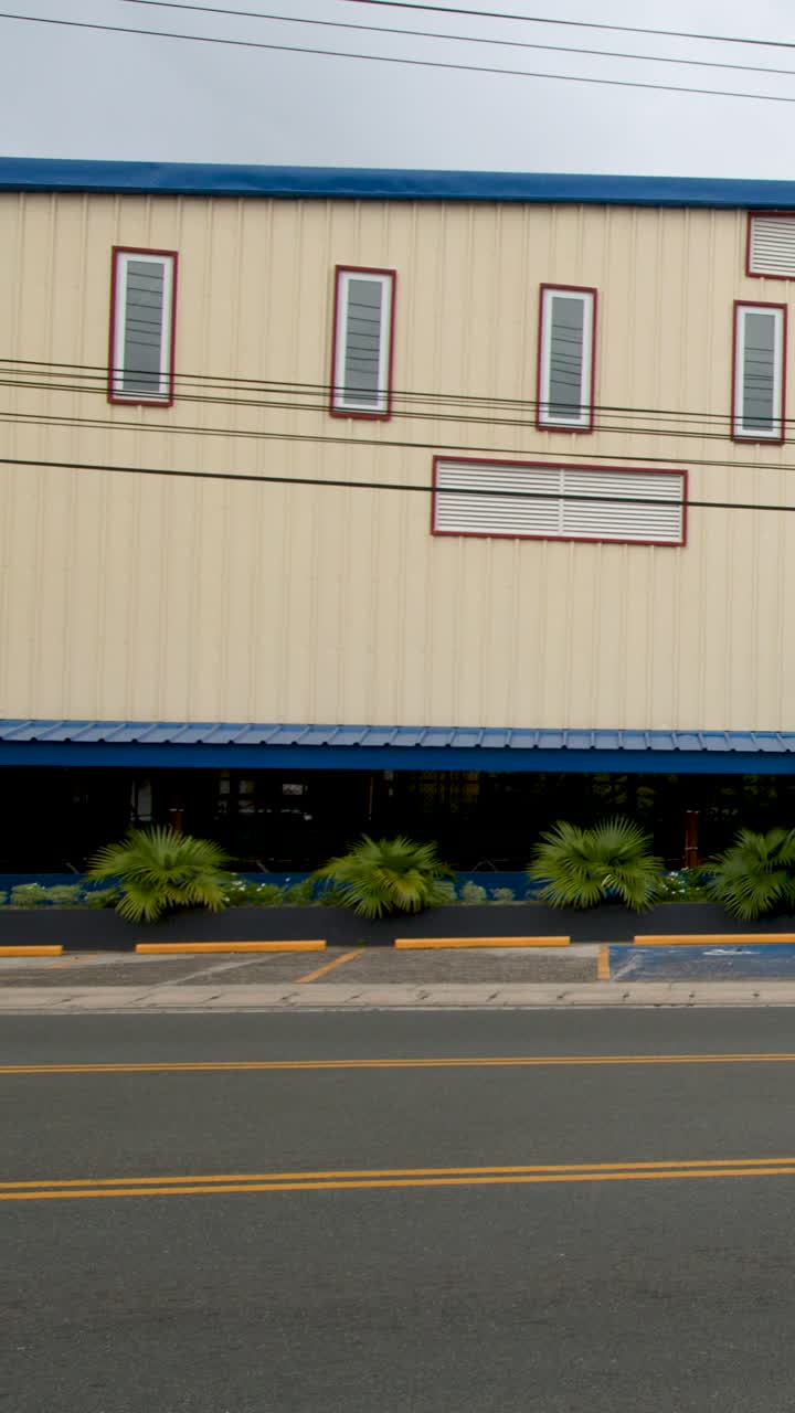 Un coche rojo circula por una calle urbana, pasando por delante de un gran edificio de instalaciones deportivas escolares.