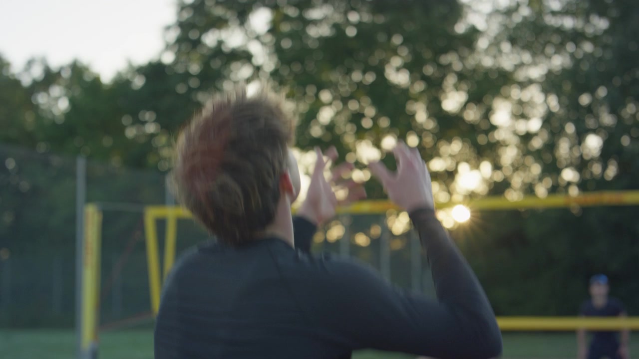 Back view of young male student playing volleyball on outdoor court at sunset, team sport training and recreation with net and warm evening light
