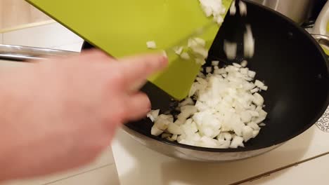 caucasian woman cooking and putting cut up onion into frying pan