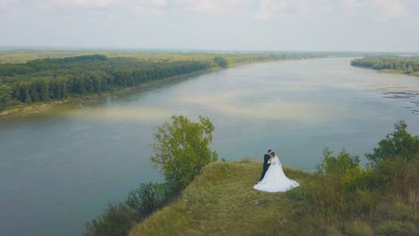 just married couple kisses on steep bank near river aerial