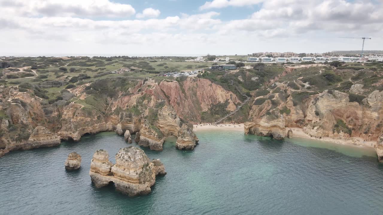 Aerial drone pulls back from Algarve beach and cliffs, showing wide coastal view near Lagos Portugal