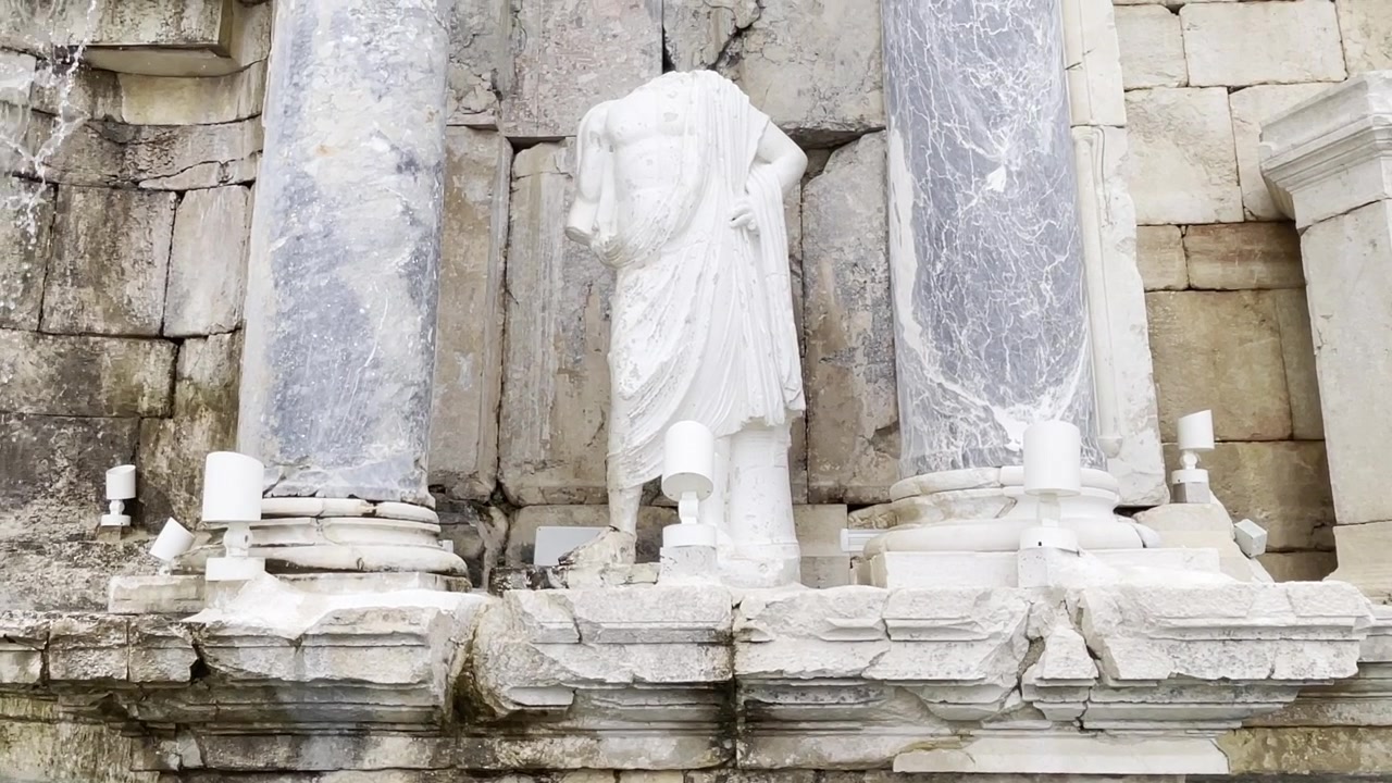 Panoramica verso l'alto dell'acqua che scorre oltre un'antica statua romana senza testa al Ninfeo Antonino a Sagalassos, Turchia.