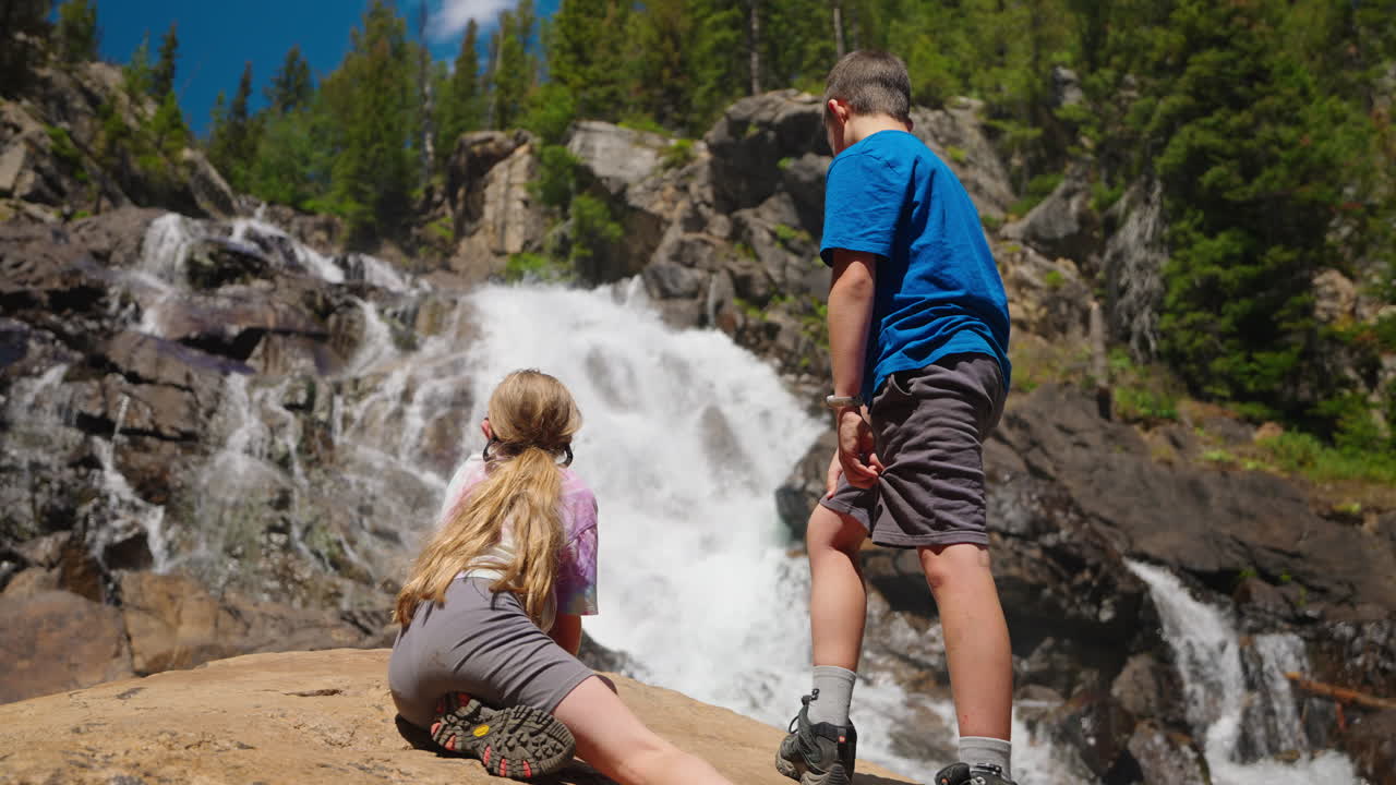Children Admiring a Majestic Waterfall in Nature