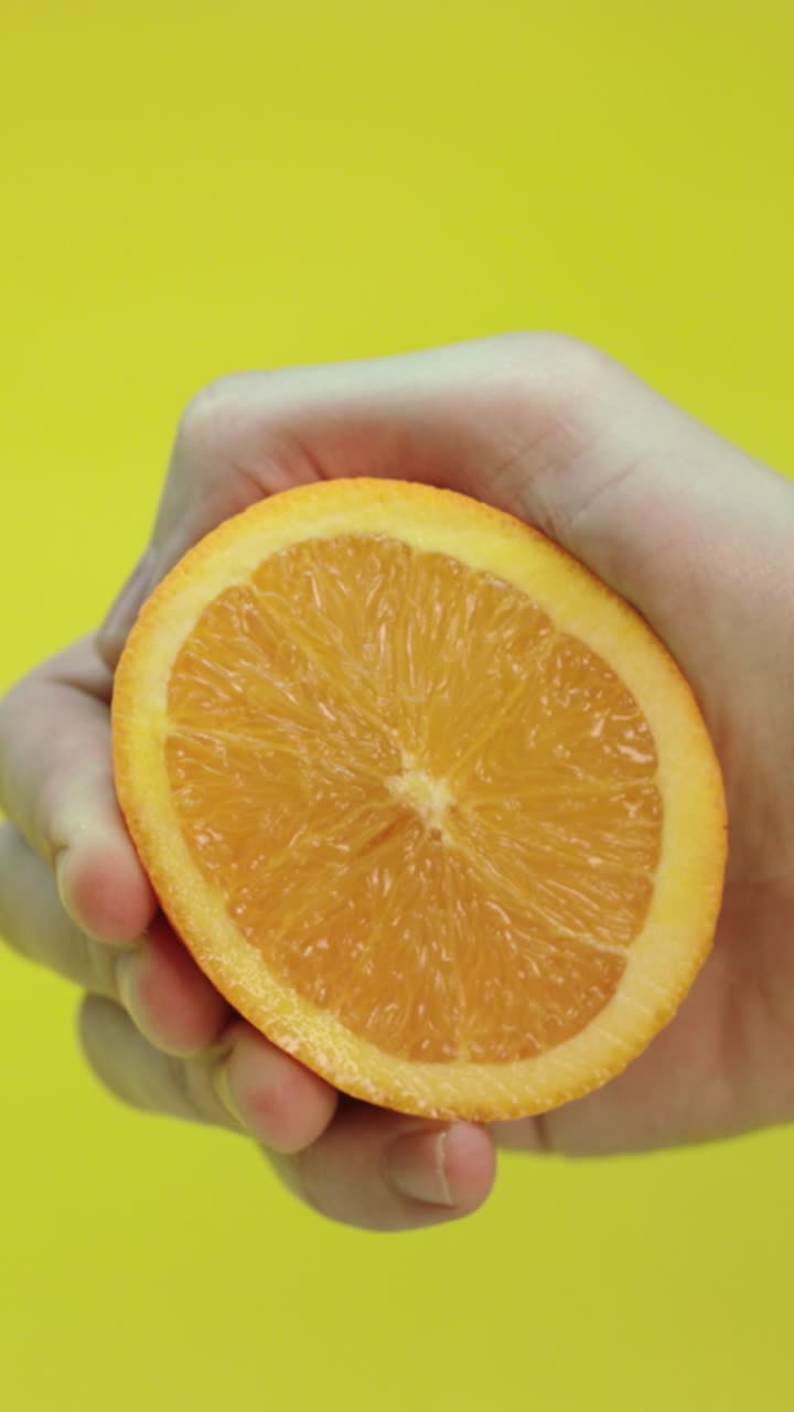 Arancia spremuta a mano con succo che schizza su sfondo giallo, primo piano al rallentatore.