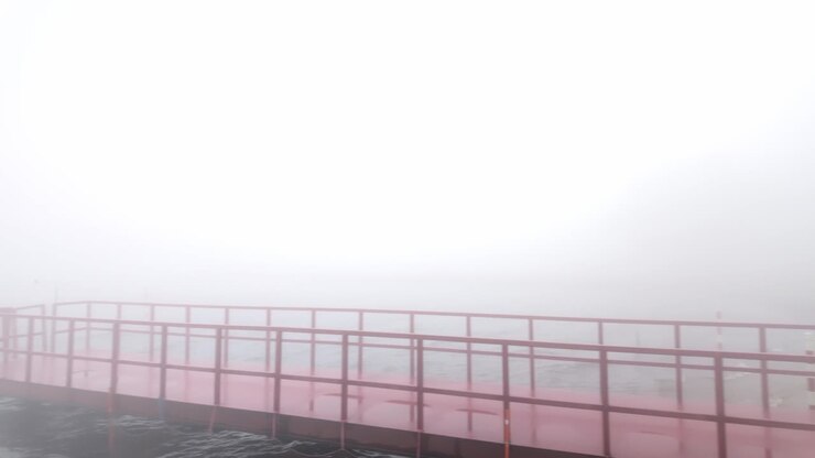 Panorâmica de um píer vermelho em um lago calmo desaparecendo em névoa densa, revelando lentamente a costa enevoada e silhuetas suaves sob a luz matinal de baixo contraste no Japão
