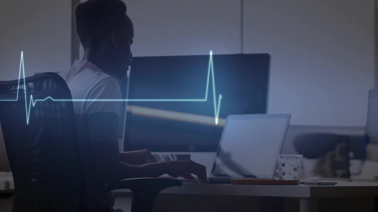 Animazione di un monitor cardiaco sullo sfondo della vista posteriore di un uomo d'affari afroamericano che usa il laptop in ufficio