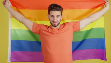 smiling man wrapped in rainbow flag on yellow background