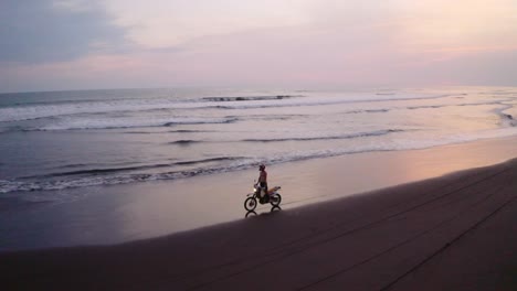 Dirtbike-Fahrer,-Der-Das-Leben-Liebt-Und-Bei-Sonnenuntergang-Am-Strand-Entlang-Kreuzt.-Rückflug-Aus-Der-Luft