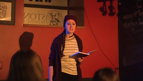 young women reads slam poetry book and walks off stage wearing red beanie