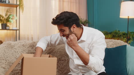 indian young excited man opening delivery package looking inside with joy unboxing online purchase