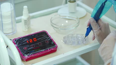 beautician is dunking special needle into a dye for coloring eyebrows on the table in a beauty salon. preparation for the procedure of permanent makeup.