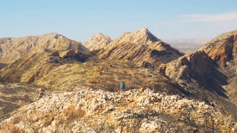 Hiker-walks-towards-jagged-mountain-landscape,-Central-Australia