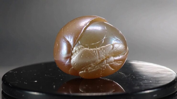 Rotating glossy pedestal turning cracked bead, revealing seam and glow on studio table for camera