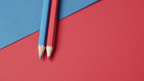 Close-up-of-blue-and-red-crayons-with-copy-space-on-red-and-blue-background,-in-slow-motion