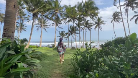 young girl in beach kimano strolls amongst towering coconut palm trees at pasut black sand beach, bali