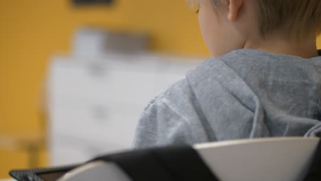 Rear-view-of-caucasian-school-boy-playing-game-on-tablet-in-classroom,-Close-up