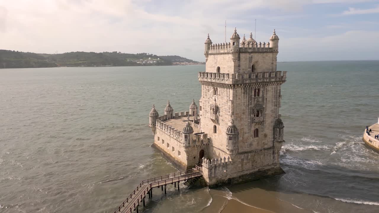 Slow aerial rotating shot of Torre de Bel&eacute;m in Lisbon with waves crashing