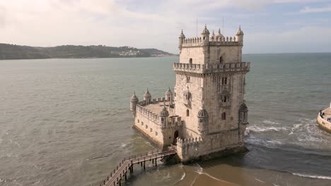 slow aerial rotating shot of torre de belém in lisbon with waves crashing