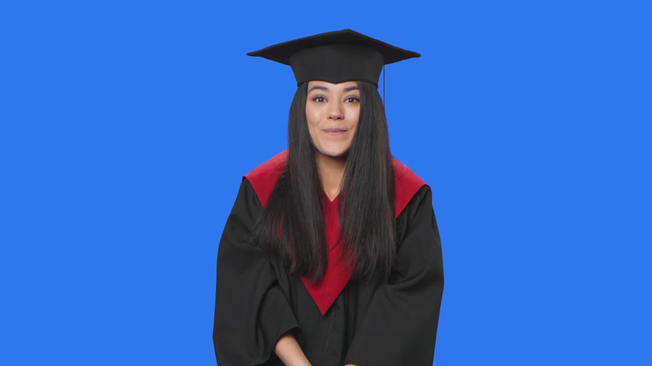 Portrait of female student in graduation costume looking at camera with wow delight and admiration. Young brunette posing in studio with blue screen background. Close up. Slow motion ready 59.94fps