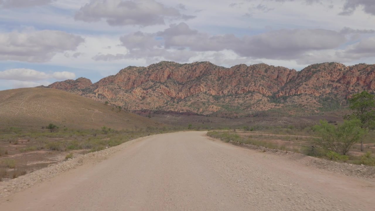 Um caminho de terra corta o outback australiano, guiando o olhar para uma cordilheira distante em Flinders Ranges.