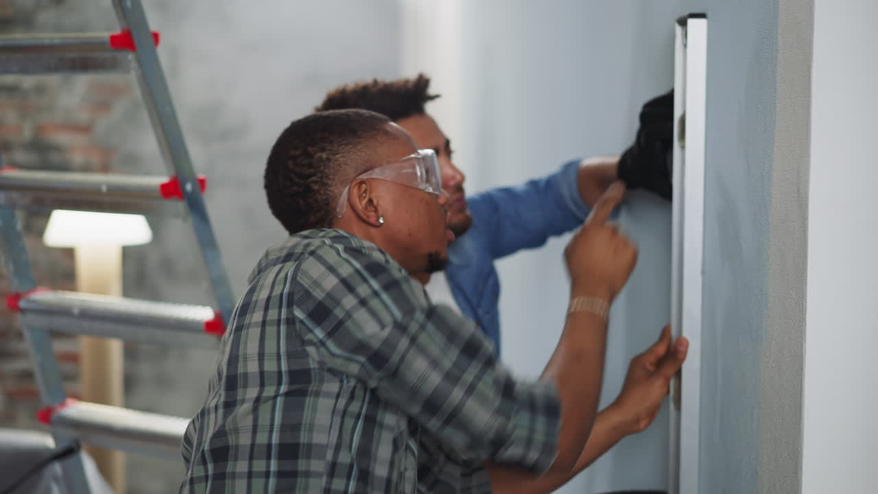 Black guys check wall with spirit level working in apartment