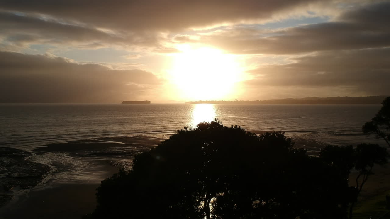 Drone footage flying towards the sunrise - Howick, east Auckland in New Zealand. Cloudy Skies with the sun breaking through with its golden beams shining down on the bays below.