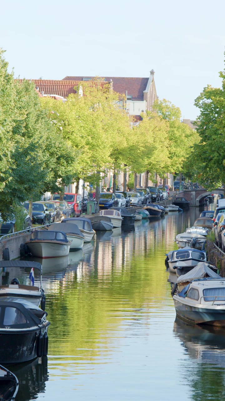 Canale urbano tranquillo con barche ormeggiate e alberi verdi.