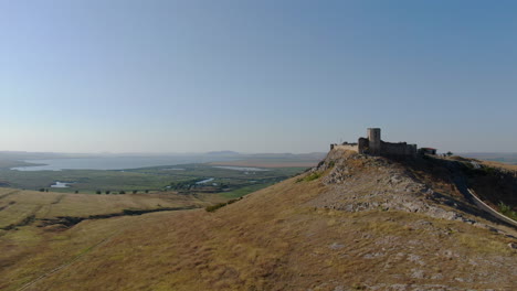 aerial drone rising shot with front side of enisala, medieval fortress on top of a hill surrounded by lakes and plains on a clear sunny day