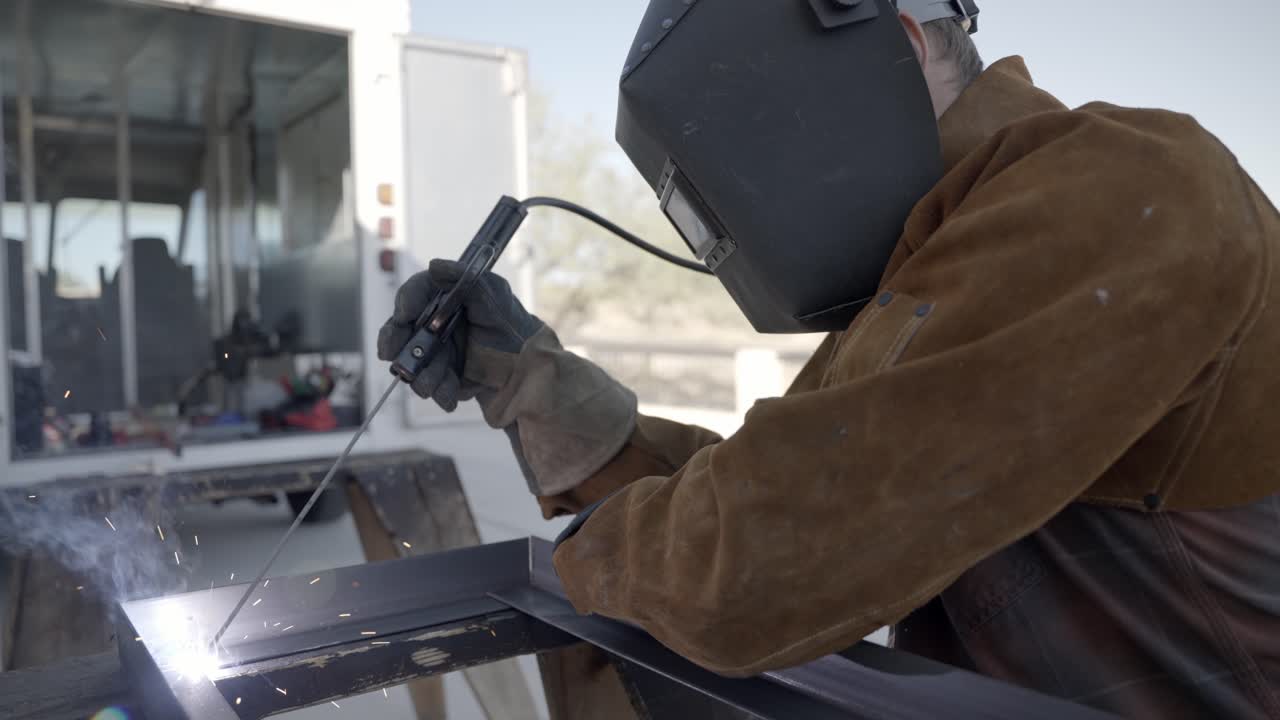 Welder welding with long rod metal construction frame wearing shield mask outdoors