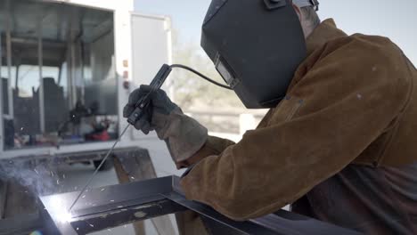 welder welding with long rod metal construction frame wearing shield mask outdoors