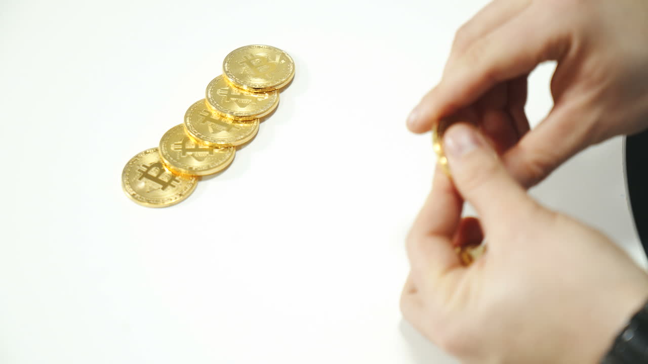 Physical real golden Bitcoin coin in men's hand - virtual crypto currency, financial concept, banknotes of different countries