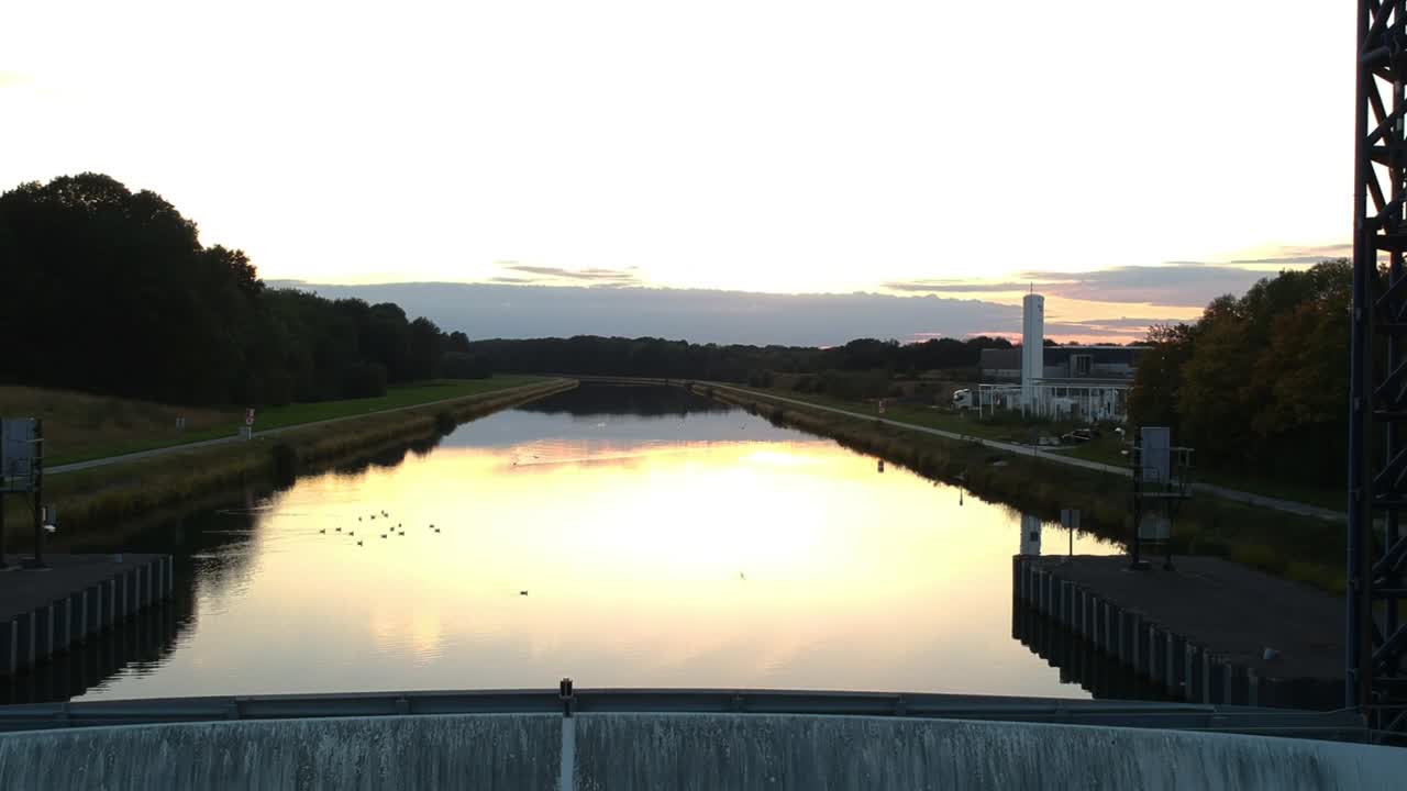 드론은 작은 새들이 일몰 속으로 날아가는 강 댐 위로 떠오른다