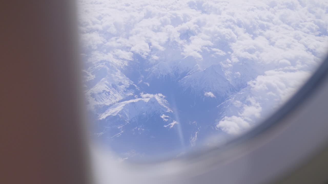 Snowy mountain peaks seen through an airplane window above the clouds