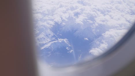 snowy mountain peaks seen through an airplane window above the clouds