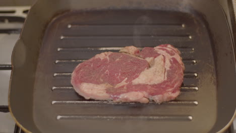 smoke rising from sizzling ribeye steak in grill pan